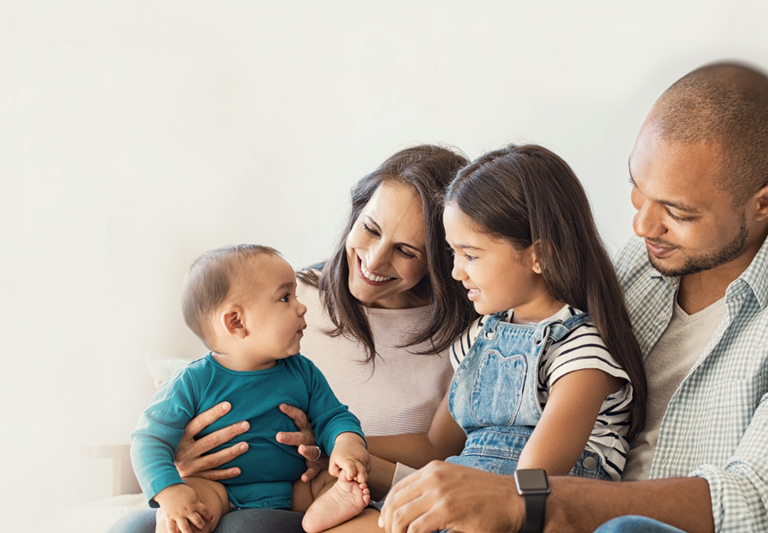 Multiethnic family. Little girl sitting on leg of dad and looking at her new cute brother sitting on mom's lap.