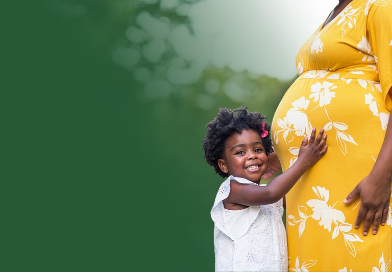 African American pregnant woman with her young daughter hugging her belly.