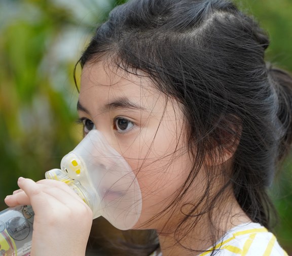 Young Asian girl with asthma using inhaler and spacer. Respiratory system and allergies