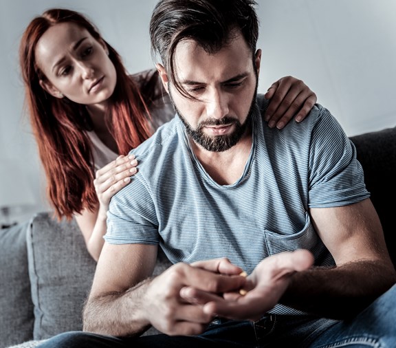 depressed man struggling with pill addiction and woman trying to comfort him