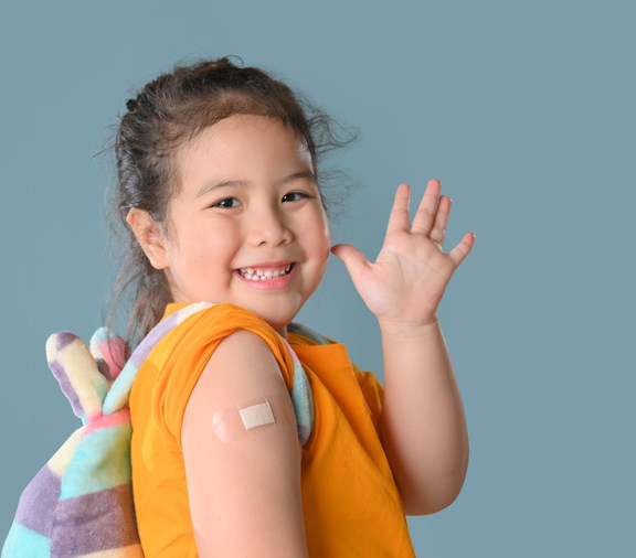Happy Vaccinated Little Asian girl Showing Arm with Plaster Bandage After Vaccine Injection, Smiling to Camera. New normal back to school concept