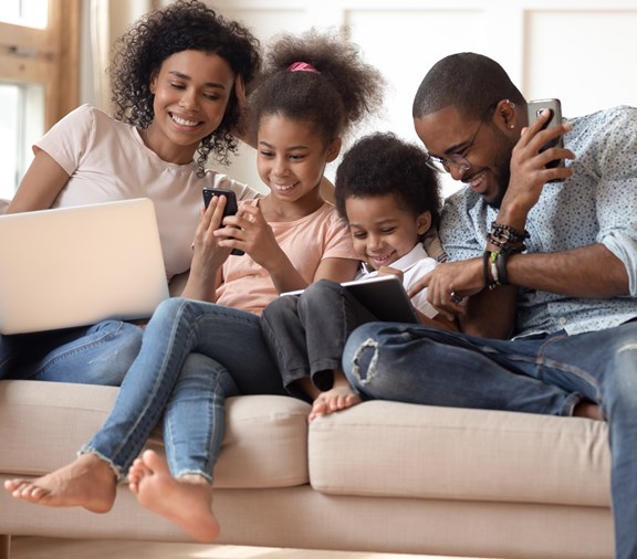 happy family sitting on couch using different technology devices