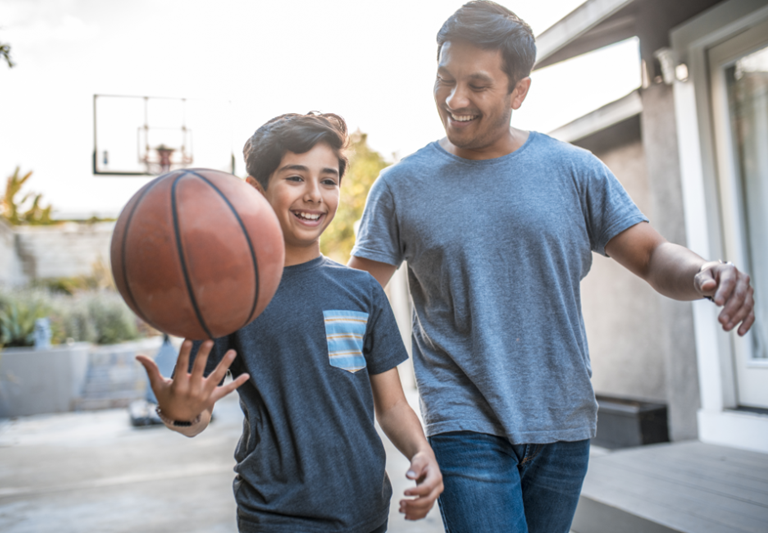 Happy boy spinning basketball while walking by father.